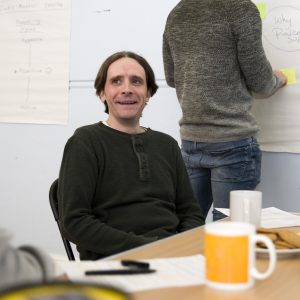 Male sitting at a table with a yellow mug on the table 