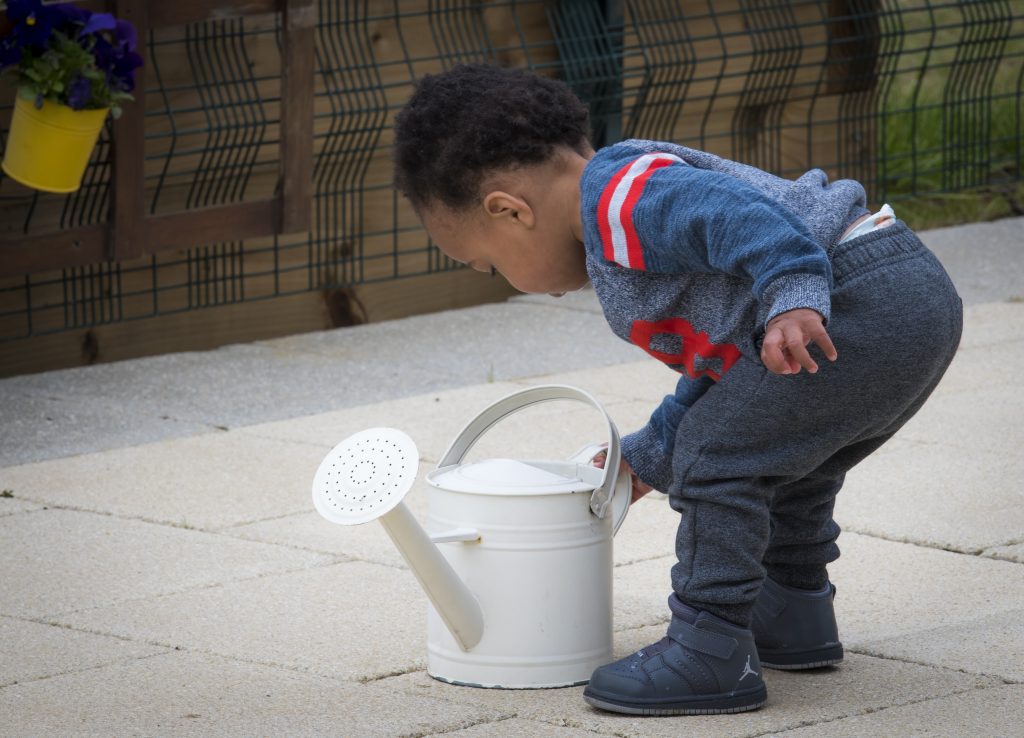 Toddler standing over a watering can 
