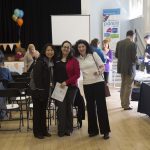 3 females smiling at the camera holding a Sharing Parenting frame in a community hall